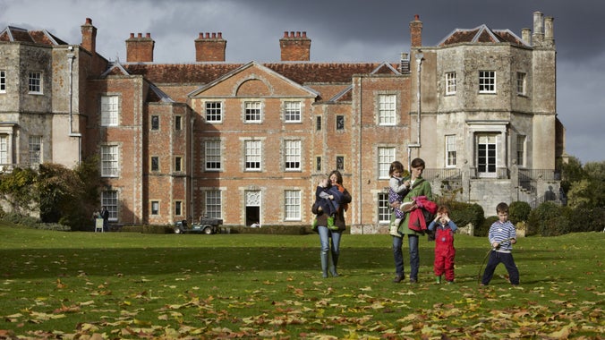 Exterior of house, with family on leaf covered autumn lawn in the foreground